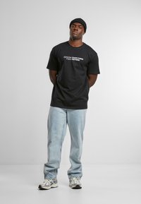 Black cotton t-shirt with white text "Appreciate EVERYTHING Expect NOTHING," paired with faded blue jeans and metallic sneakers.