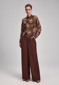 Langærmet bluse med blomsterdesign i grøn, pink og brun; kombineret med højtaljede, brede brune bukser og spidse beige hæle.