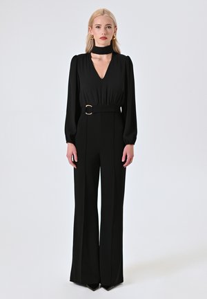 Jumpsuit nero con maniche a sbuffo lunghe, scollo a V e vita con cintura caratterizzata da una fibbia dorata. Tessuto liscio; design con pantaloni a gamba larga.