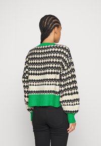 Zkrácený svetr s černým, bílým a zeleným diamantovým vzorem. Žebrovaný zelený lem a manžety; texturovaný pletený materiál. Zobrazeno z zadní strany.