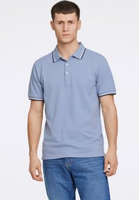 Lyseblå polo shirt med mørkeblå kant på kraven og ærmerne, der har en tre-knapps placket og broderet logo på brystet.