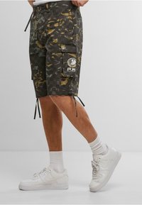 Camouflage cargo shorts with a black, yellow, and green pattern, featuring multiple pockets and drawstring hems, paired with white sneakers.