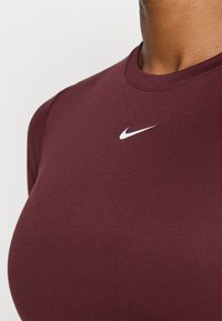 Camiseta atlética ajustada burdeos hecha de una tela suave, con el logo de Nike en blanco en el pecho y un cuello redondo.