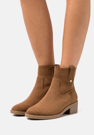 Braune Wildleder-Stiefeletten mit runder Zehenform, niedrigem Blockabsatz, seitlichem Reißverschluss und dekorativer Nahtakzentuierung.