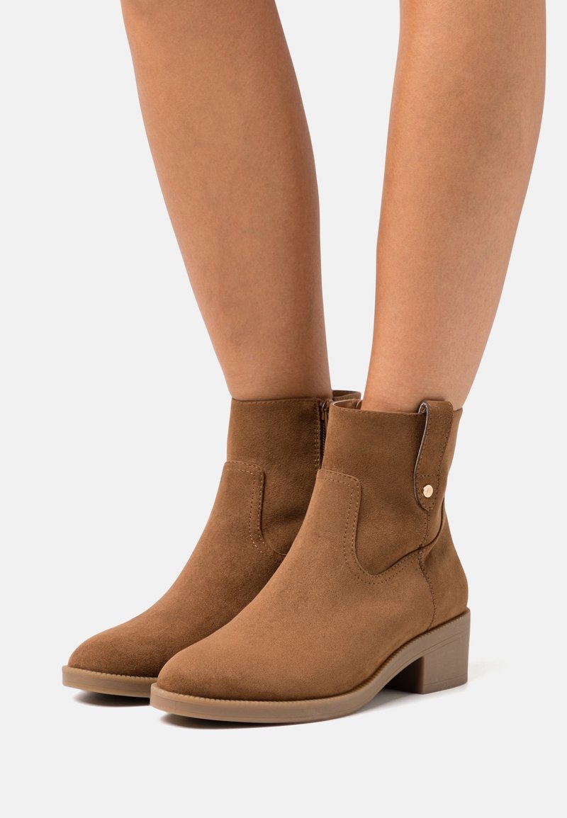 Braune Wildleder-Stiefeletten mit runder Zehenform, niedrigem Blockabsatz, seitlichem Reißverschluss und dekorativer Nahtakzentuierung.