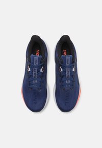 Baskets de sport bleues avec une tige en maille texturée, des accents noirs et une semelle blanche avec un détail orange au talon.