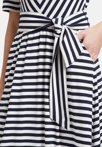 Navy- und weiß gestreiftes Kleid mit tailliertem Oberteil, ausgestelltem Rock und einem gebundenen Taillengürtel, seitlicher Tasche und glatter Textur.