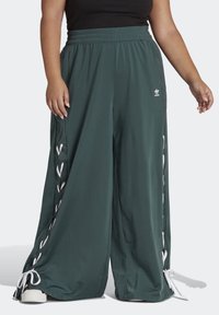 Zelené široké kalhoty vyrobené z hladké látky, s bílým šněrováním po stranách a nařaseným elastickým páskem.
