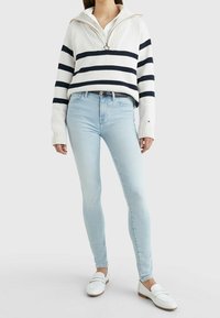 Bílý a námořnický pruhovaný svetr se zipovým límcem, doplněný o světle modré skinny džíny a bílé mokasíny, představující ležérní outfit.