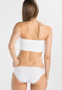 Bílý bandeau top a odpovídající bikini spodní díl, vyrobený z hladké látky, s jednoduchým designem a minimalistickým střihem, zobrazený zezadu.