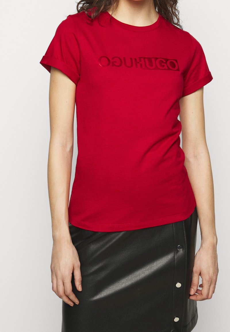 Femme portant un t-shirt rouge à manches courtes avec revers pliés et une jupe en cuir noire avec des boutons-pression latéraux.
