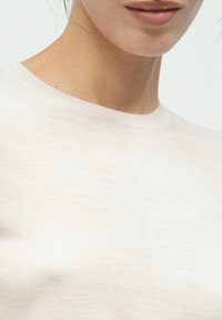 Top beige chiaro con scollo rotondo, realizzato in tessuto morbido, caratterizzato da una trama liscia e un design semplice, con dettagli minimi visibili.