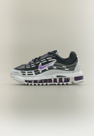 Baskets Nike Max Air noir et blanc avec des touches violettes et un amorti à air visible dans la semelle, vues de côté sur un fond uni.