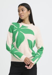 Hellrosa Pullover mit großem grünem Blattmuster, Rundhalsausschnitt, langen Ärmeln, flauschiger Textur und gerippten Bündchen.