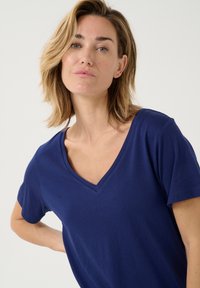 Námořnická modrá tričko s krátkým rukávem a véčkovým výstřihem. Měkká tkanina, uvolněný střih a jednoduchá konstrukce bez vzorů nebo ozdob.