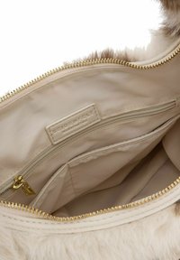 Intérieur d'un sac à main en fausse fourrure beige avec une doublure lisse, fermeture éclair dorée, et deux poches compartimentées, dont une zippée. Étiquette de marque visible.