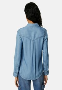 Lichtblauwe denimbloes met een klassieke kraag, lange mouwen en een licht afgeronde zoom. Bevat een rug yoke en knoopmanchetten.