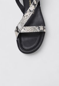 Sandale noire avec des brides croisées au motif serpent, texture contrastante et matériau lisse sur la semelle.