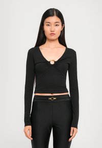 Black long-sleeve top featuring a V-neck with a gold ring accent at the center, made from a smooth, stretchy material.