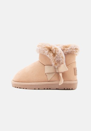 Stivaletti alla caviglia in suede beige con colletto in pelliccia sintetica, rifiniti con un fiocco in tessuto e una suola in gomma testurizzata per una buona aderenza.