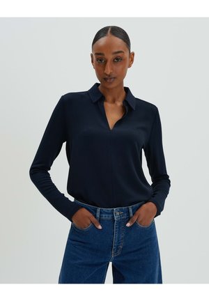 Marineblaue Bluse mit langen Ärmeln, Kragen und V-Ausschnitt. Aus glattem Stoff gefertigt, kombiniert mit hoch taillierten blauen Denim-Jeans.