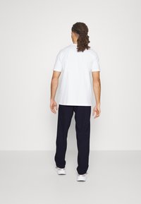 White short-sleeve t-shirt paired with navy blue sweatpants. The outfit features a relaxed fit and minimalistic design. White athletic shoes.