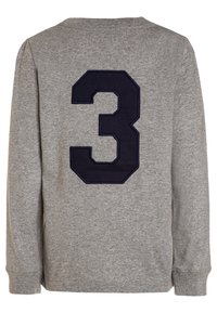 Šedá dlouhá rukávová košile s kulatým výstřihem a aplikací námořnicky modré číslo "3" na zadní straně. Vyrobeno z měkké texturované tkaniny.