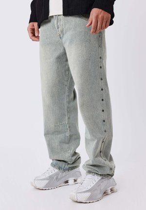 Lichtgroene baggy jeans van denim, met een knoopsluiting aan de zijkant en een relaxed fit, gecombineerd met witte sneakers.