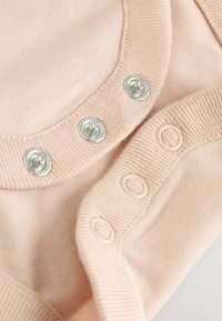 Jasnoróżowy materiał o gładkiej fakturze; posiada metalowe zatrzaski i miękkie prążkowane krawędzie. Z boku znajdują się dopasowane plastikowe zatrzaski.