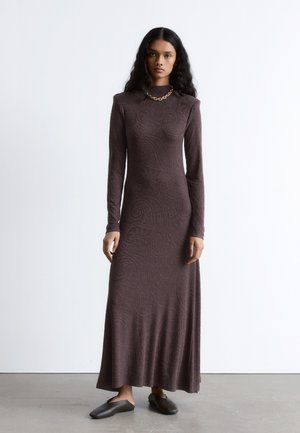 Brown, long-sleeve dress with a floor-length skirt and paisley pattern. Smooth fabric, high neck, and subtle texture. Paired with dark slip-on shoes.
