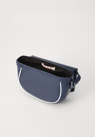 Geantă sintetică de culoare albastru marin, cu un design curbat, cusături albe și curea ajustabilă. Partea superioară deschisă dezvăluie un interior negru și un eticheta interioară.