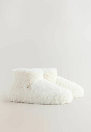 Mehki, beli, puhasti copati do gležnjev z majhno tekstilno oznako na strani, prikazani na preprostem svetlem ozadju.