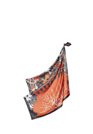 Foulard carré en soie avec des motifs floraux orange, noir et gris, noué à un coin, suspendu sur un fond blanc.