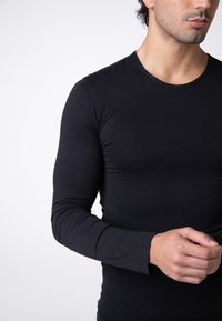 Maglietta nera a maniche lunghe realizzata in tessuto morbido e elasticizzato. Presenta un colletto rotondo e un design aderente, che mette in risalto la silhouette di chi la indossa.
