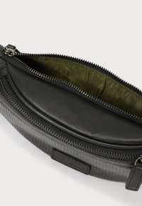 Μαύρο υφασμάτινο νεσεσέρ με φερμουάρ και εσωτερική επένδυση από ελαιώδες πράσινο ύφασμα, εμφανισμένο μισοανοιγμένο σε λευκό φόντο.