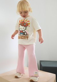 Biała bawełniana koszulka z kolorowym nadrukiem Hello Kitty, w zestawie z miękkimi różowymi spodniami w prążki, z metką z motywem Hello Kitty i akcentami.
