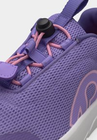 Približna snimka ljubičaste tenisice od mrežastog materijala s ružičastim elastičnim vezicama pričvršćenim crnim klizačem na bijelom potplatu.