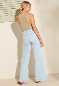 Lichtblauwe flared jeans in combinatie met een gouden geribbelde tanktop. De outfit heeft een gestructureerd uiterlijk en een casual silhouet.