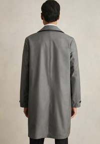 Palton gri cu un design ajustat, având o deschidere la spate, manșete cu nasturi și o textură netedă. Linii curate și un croi până la genunchi.