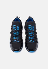Μαύρα αθλητικά παπούτσια με γυαλιστερό, υφή επιφάνειας. Μπλε τυπωμένο κείμενο στα πλευρά. Σχέδιο με κορδόνια, μπλε εσωτερικό και ευέλικτη σόλα.