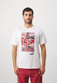 Valge puuvillane T-särk, millel on värvikas graafiline disain punaste, mustade ja valgete mustritega, mis on keskendunud "RB Leipzig"-ile. Sisaldab Puma logo.