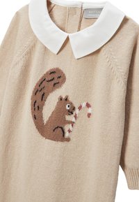 Pull en tricot beige avec un col blanc présentant un motif de écureuil tricoté tenant un sucre d'orge. Il a une texture douce et une coupe décontractée.