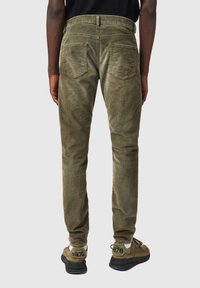 Pantalones de corduroy verde oliva con un ajuste slim, diseño de cinco bolsillos y detalles de textura sutil, combinados con zapatillas grises con acentos negros.