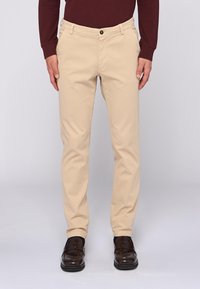 Beige Chinos in schlanker Passform, gefertigt aus leichtem Stoff. Verfügt über einen klassischen Knopfverschluss, Gürtelschlaufen und Seitentaschen.