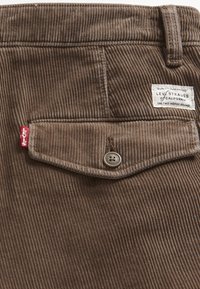 Pantaloni in velluto a coste marroni con una tasca posteriore, bottone in ottone e un'etichetta bianca con la scritta "Levi Strauss" e un tab rosso.