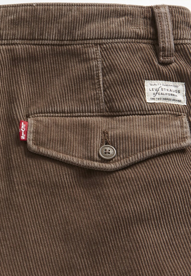 Braune Cord-Hosen mit einer Gesäßtasche, einem Messingknopf und einem weißen Etikett mit der Aufschrift "Levi Strauss" und einem roten Akzenttab.