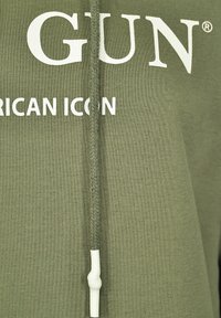 Zielona bluza z kapturem z białym napisem "GUN" oraz "AMERICAN ICON". Posiada pleciony sznurek z plastikowym końcem. Miękki materiał, casualowy design.