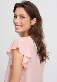 Helles rosa Bluse mit gerafften kurzen Ärmeln, weichem Stoff und lässiger Passform. Der Ausschnitt ist rund und das Gesamtdesign ist einfach.