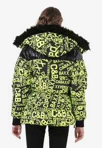 Zwarte en neon groene pufferjack met gedurfde tekstpatronen, faux fur afwerking op de capuchon en ribgebreide mouwen. Textuur oppervlak met glanzende accenten.