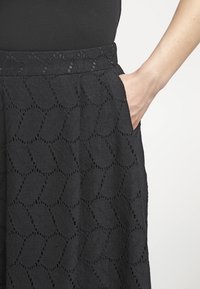 Zwarte stoffen rok met een ingewikkeld bladvormig patroon, gekreukt weefsel en zichtbare zijzak. De tailleband ligt plat tegen het lichaam.